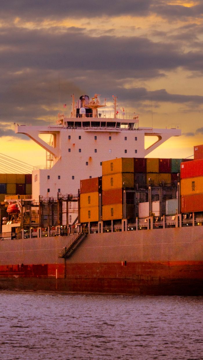 Cargo ship loaded with colorful containers against a vibrant sunset sky.